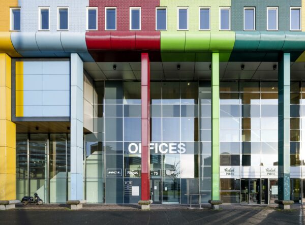 Ingang van een kleurrijk kantoorgebouw aan de Johan Cruijff Boulevard met grote glazen gevel en gekleurde zuilen.